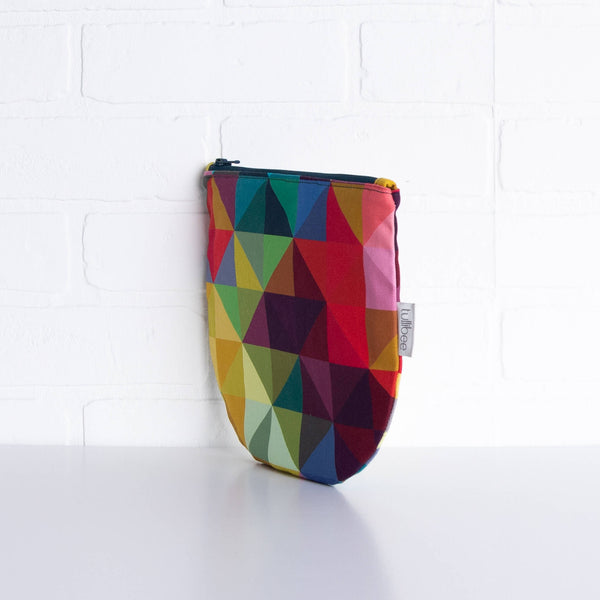 tullibee jules rainbow geometric triangle midi round pouch propped upright against a white brick wall at an angle to show the depth of the pouch