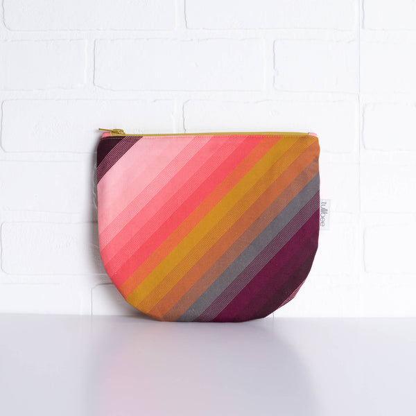 tullibee agnes tonal diagonal stripe midi round pouch propped against a white brick wall (front view)