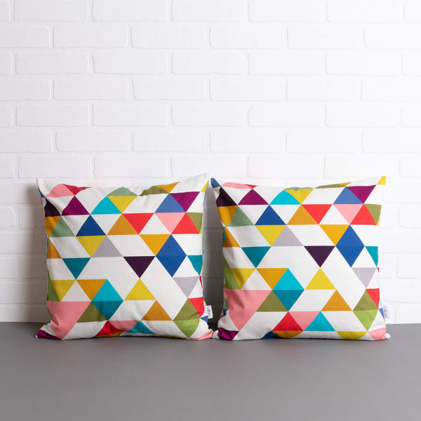 two tullibee Yoshi triangle geometric rainbow colour cushions sat side by side on a concrete floor in front of a white brick wall