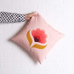tullibee margot in the middle large retro floral cushion, in cherry flamingo & mustard colours being held out by a arm with a black & white spotty shirt