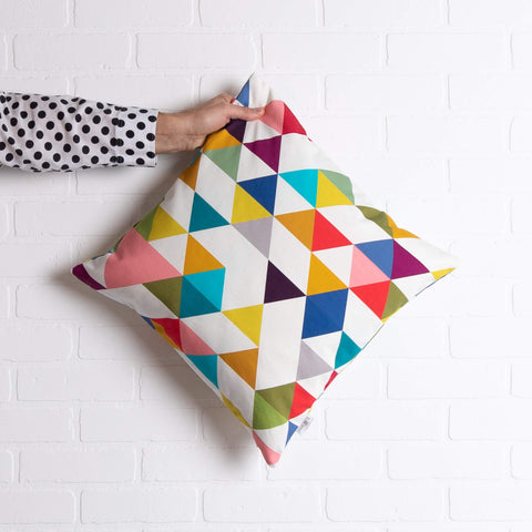 tullibee yoshi triangle geometric rainbow colour cushion being held out by an arm with a black & white spotty shirt