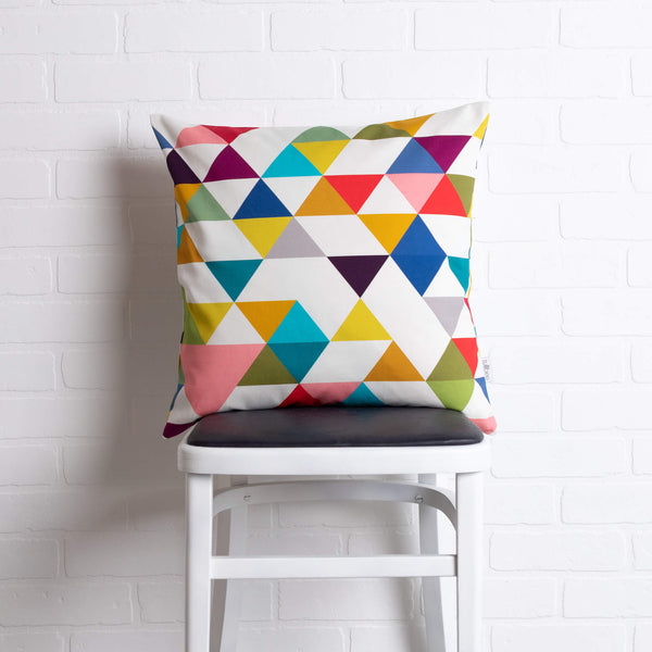 tullibee yoshi triangle geometric rainbow colour cushion sat on a stool in front of a white brick wall
