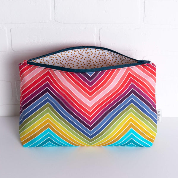 tullibee marni rainbow zig-zag maxi pouch in front of a white brick wall with zip top open & view of mustard spot lining