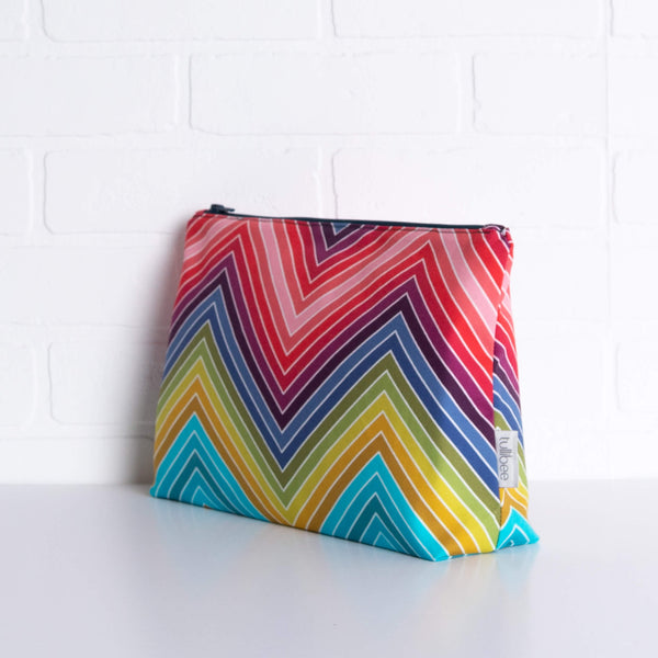 tullibee marni rainbow zig-zag maxi pouch in front of a white brick wall at an angle to show the depth of the pouch & gusset