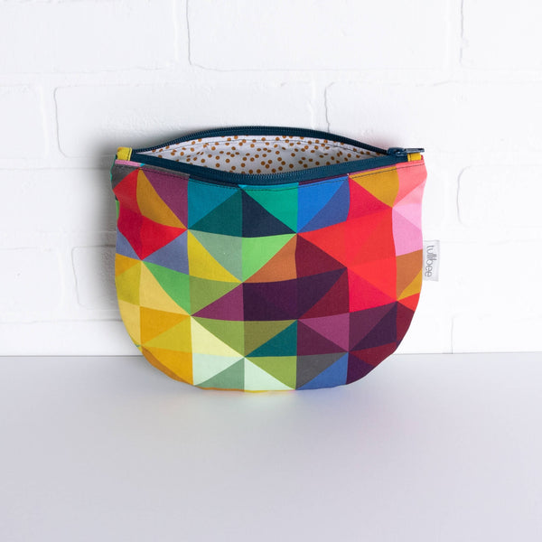 tullibee jules rainbow geometric triangle midi round pouch propped against a white brick wall with zip top open & view of mustard spot lining