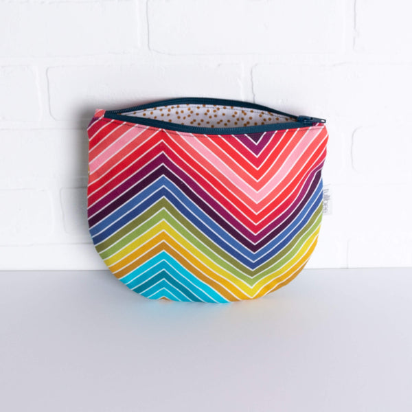 tullibee marni rainbow zig-zag midi round pouch propped against a white brick wall with zip top open & view of mustard spot lining