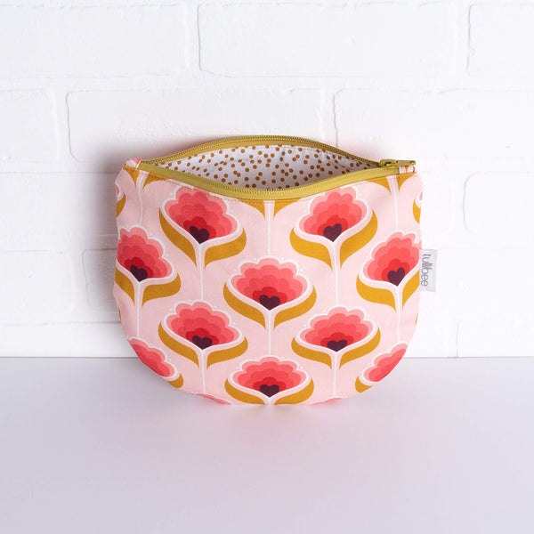 tullibee mini margot retro floral midi round pouch propped against a white brick wall with zip top open & view of mustard spot lining