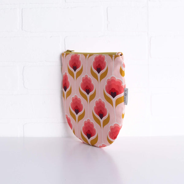 tullibee mini margot retro floral midi round pouch propped upright against a white brick wall at an angle to show the depth of the pouch